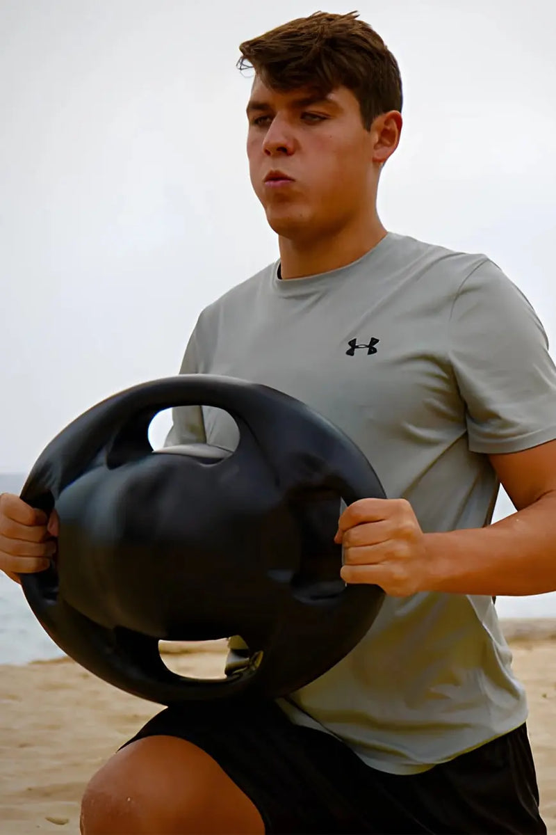 Woman using Vasspod exercise band on beach in a lunge pose, showcasing portable fitness gear for outdoor and aquatic workouts.